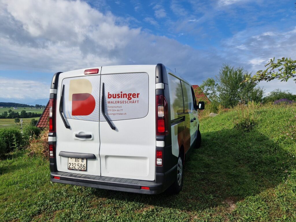 Weisser Firmentransporter mit Businger-Logo auf einer Wiese vor grünen Feldern