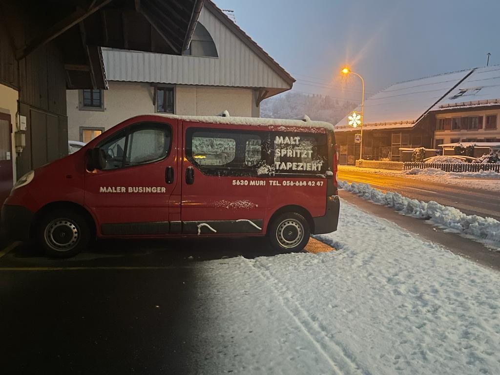 Roter Firmentransporter von Businger am verschneiten Strassenrand in der Dämmerung