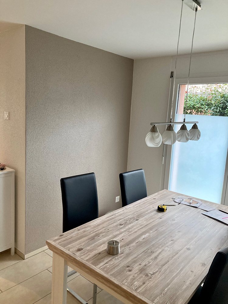Essbereich mit graubeige gestrichener Strukturwand, Holztisch und Pendelleuchte