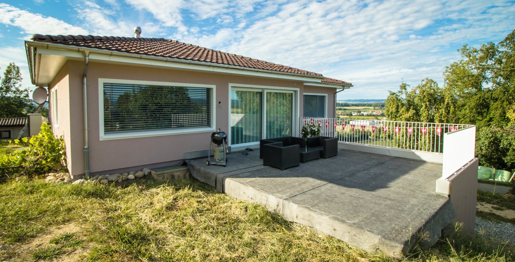 Flacher Wohnbau mit altrosa Fassade und Betonterrasse mit Blick ins Grüne