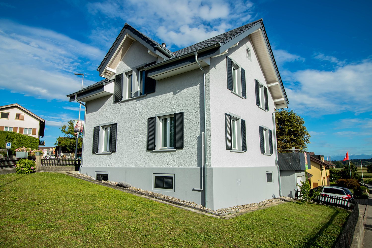 Frisch gestrichenes Einfamilienhaus mit hellgrauer Fassade und dunklen Fensterläden