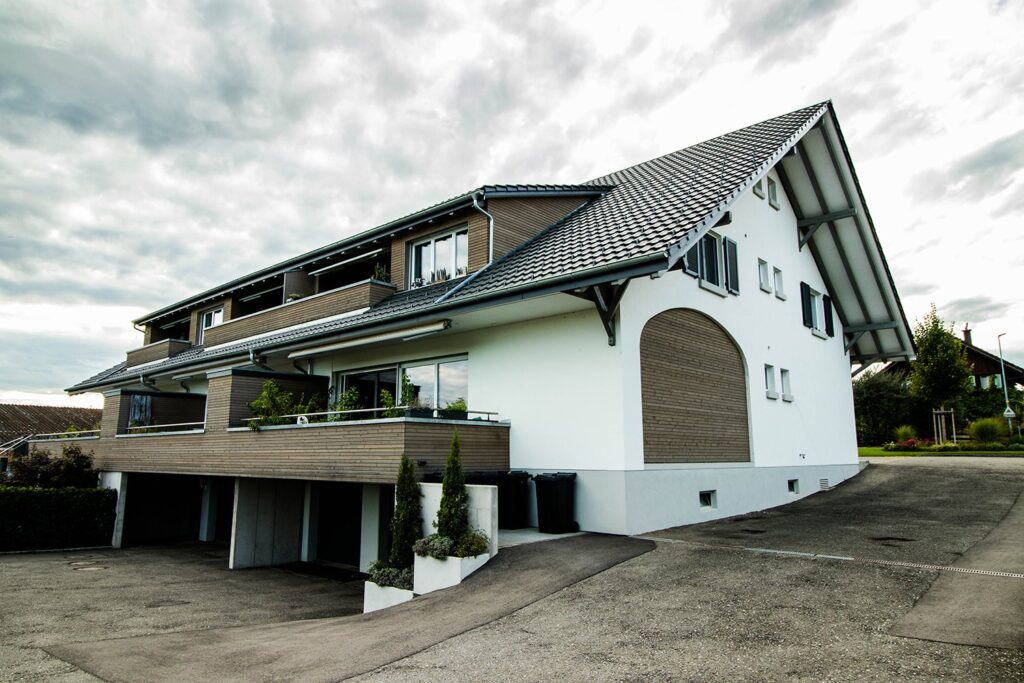 Modernes Mehrfamilienhaus mit weiss verputzter Fassade, Holzverkleidung und Balkonen