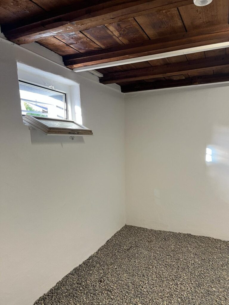Frisch weiss gestrichener Kellerraum mit dunkler Holzbalkendecke und Kippfenster