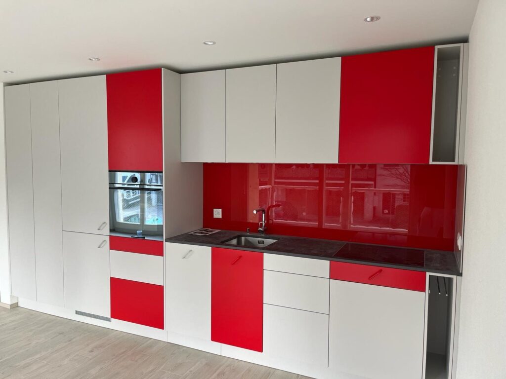 Küchenzeile mit weissen und rot glänzenden Fronten sowie roter Glasrückwand