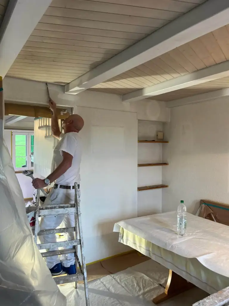 Maler zieht auf der Leiter mit der Glättkelle eine frisch gespachtelte Wand ab