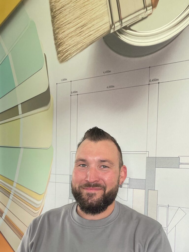 Andreas Stöckli vor einer Wand mit Farbfächern und Bauplan