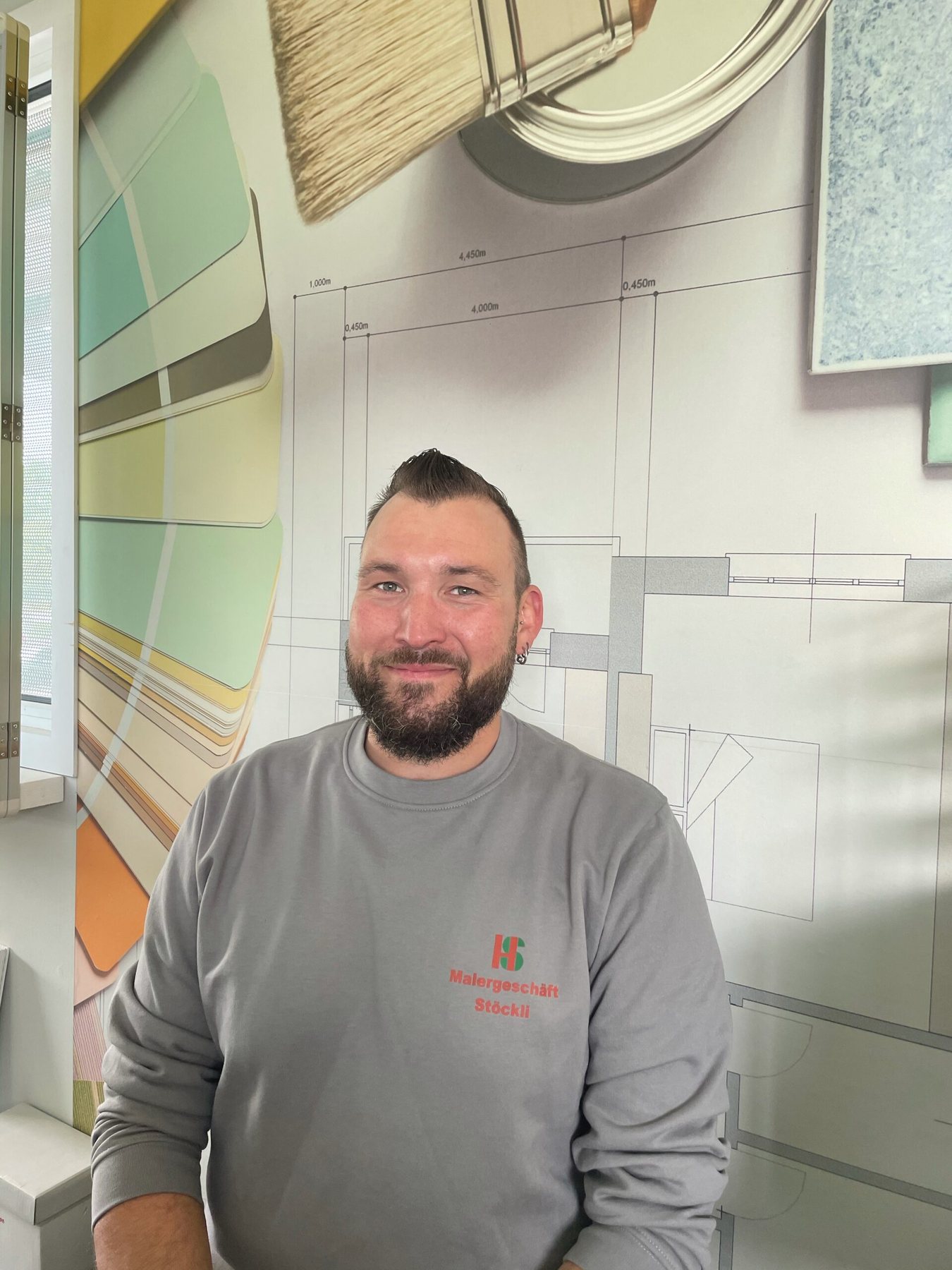 Andreas Stöckli im grauen Firmenpullover vor einer Wand mit Farbfächern