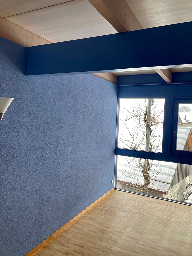 Wohnraum mit wolkig blau gestalteter Wand und blau gestrichenem Deckenbalken