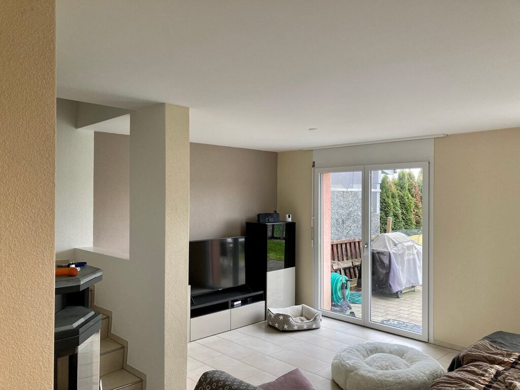 Wohnzimmer mit beige gestrichenen Wänden, weisser Decke und grosser Fenstertür
