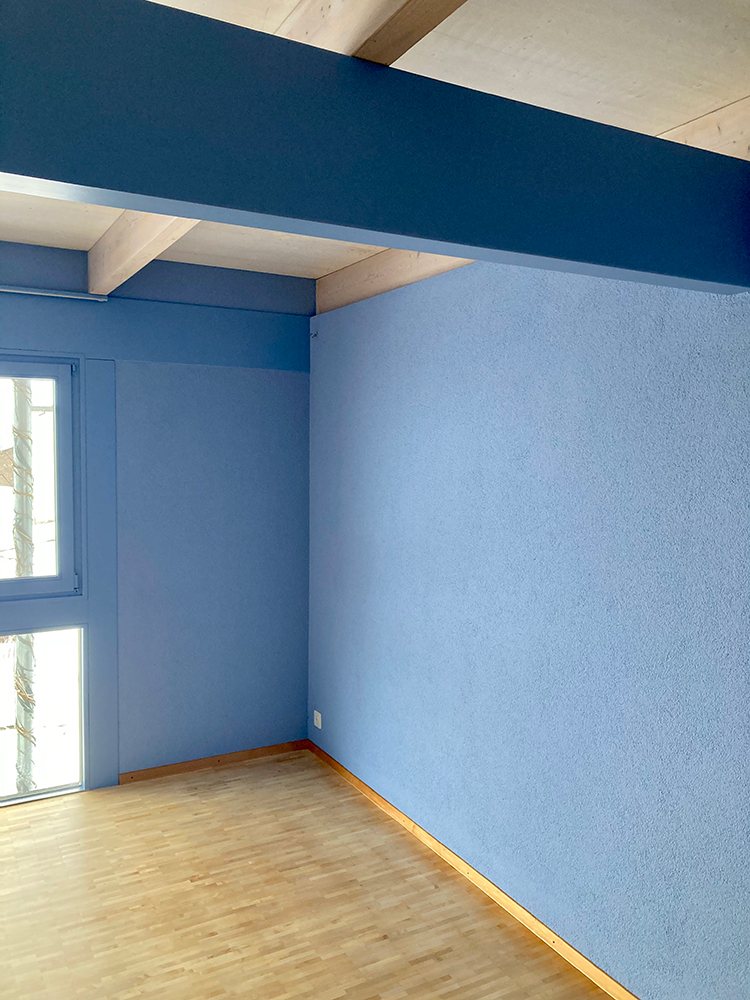 Leeres Zimmer mit blau gestrichenen Rauputzwänden und hellem Parkettboden