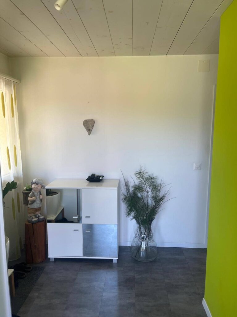 Eingangsbereich mit schlichter weisser Wand, Sideboard und Bodenvase unter einer hellen Holzdecke