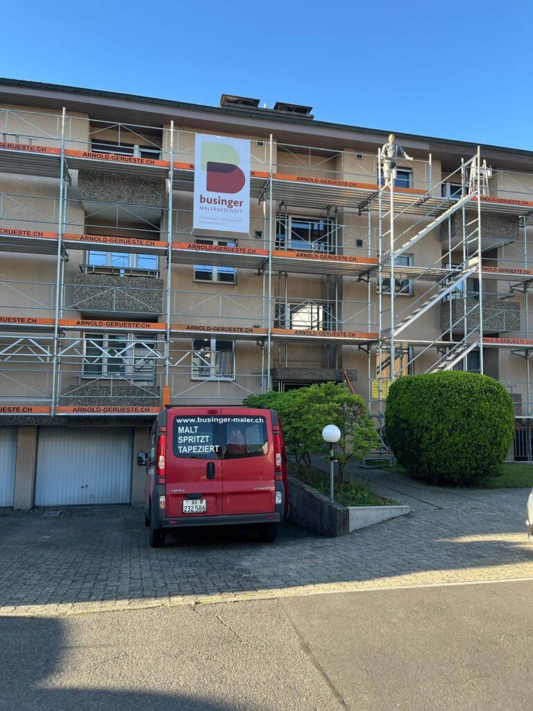 Eingerüstetes Mehrfamilienhaus mit Businger-Blache am Gerüst und rotem Firmenwagen davor
