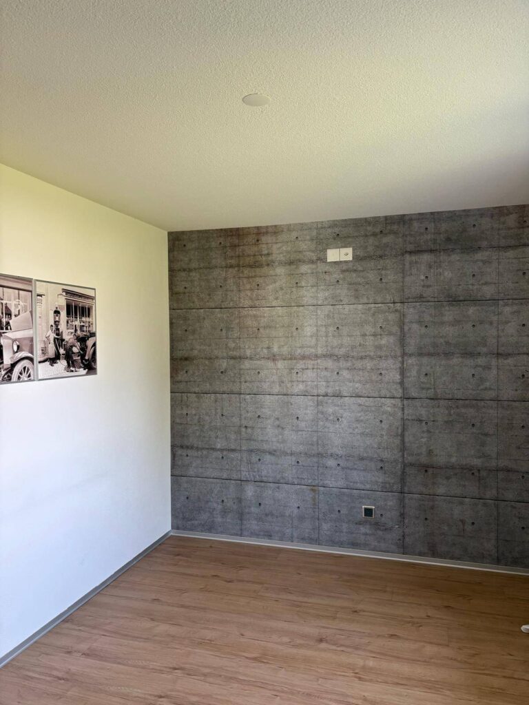 Dieselbe Wohnzimmerwand nach dem Tapezieren mit grossformatiger Tapete in Sichtbetonoptik