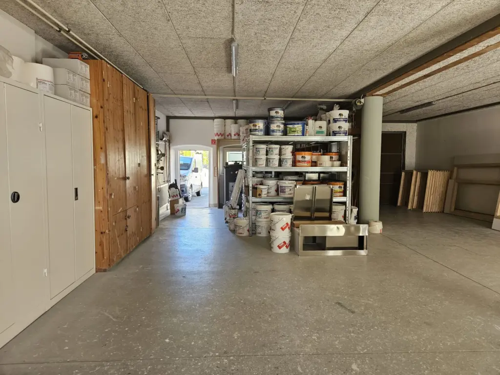 Lagerhalle von Businger Malergeschäft mit Regal voller Farbkübel, Schränken und Holzplatten