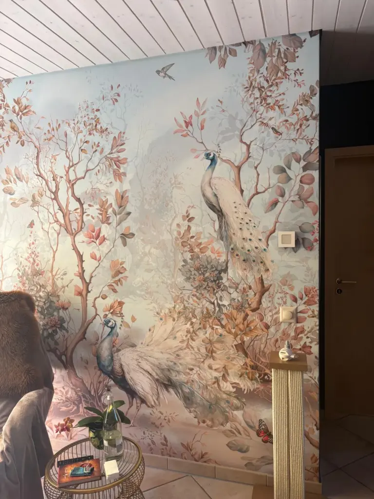 Wohnzimmerwand mit grossflächiger Fototapete mit Pfauen und Zweigen in Rosé- und Blautönen